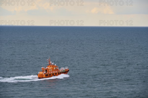 An orange pilot boat sailing on the open sea under a cloudy sky, Kiel, Schleswig-Holstein, North