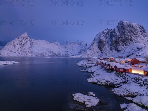 Rorbuer huts of Hamnoy at the fjord at dusk, snowy mountains in the background, Hamnøy, Reine,