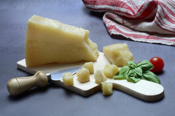 A piece of Parmesan cheese and chopped pieces of cheese on a wooden board