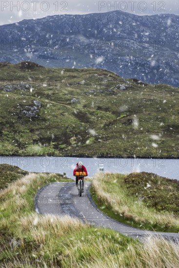 Lonely biker cycling through the Scottish Highlands on heavily laden touring bicycle along single