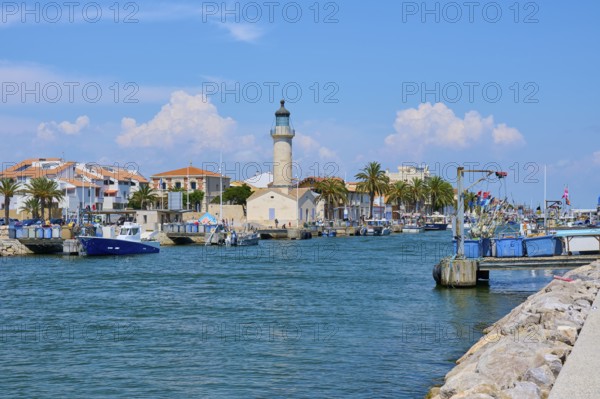 Coastal town with colourful houses and palm trees, boats in the water and a lighthouse, on a sunny