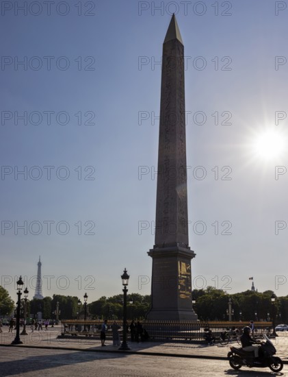Sunbeams behind an obelisk, Eiffel Tower in the background, a motorbike passing by, Paris