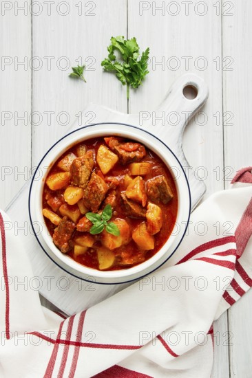 Potatoes stewed with meat, in tomato sauce, with spices and herbs, no people, on a white table