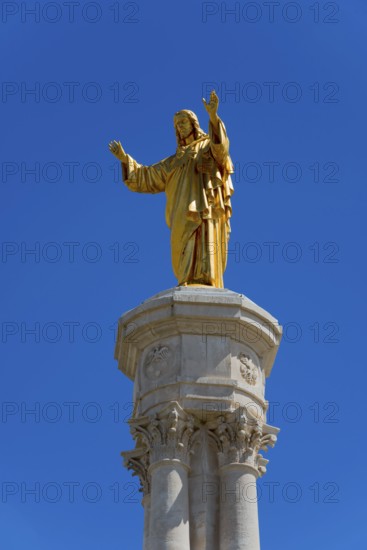 Golden statue of Jesus on a high column in front of a blue sky, Christ statue, Santuario de Fatima,