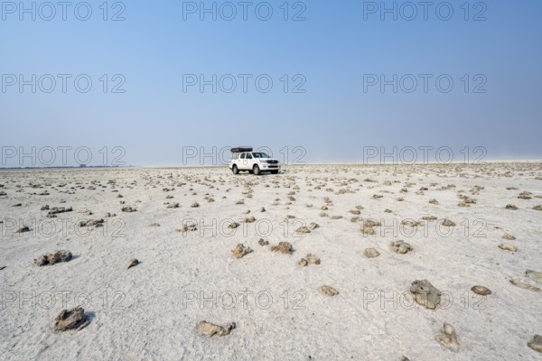 Four-wheel drive Toyota Hilux with roof tent, driving over salt pan, lone car in large wide plain,
