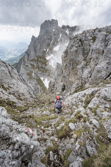 Mountaineer with helmet on a narrow hiking trail, ascent to the Maukspitze, clouds moving around