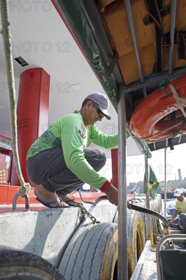 Brazilian man refuelling a boat from a floating petrol station on the Rio Negro, Manaus, Amazonas