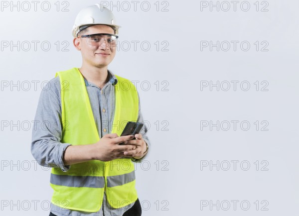 Smiling engineer holding phone looking at camera. Latin male engineer using phone isolated. Young