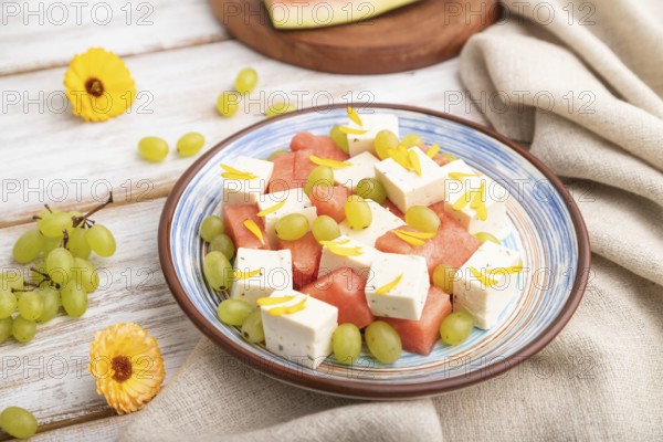 Vegetarian salad with watermelon, feta cheese, and grapes on blue ceramic plate on white wooden