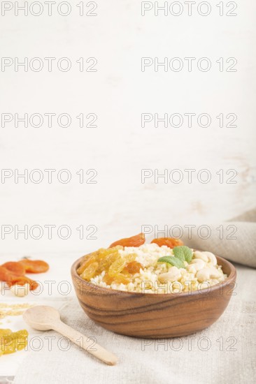 Bulgur porridge with dried apricots, raisins and cashew in wooden bowl on a white wooden background