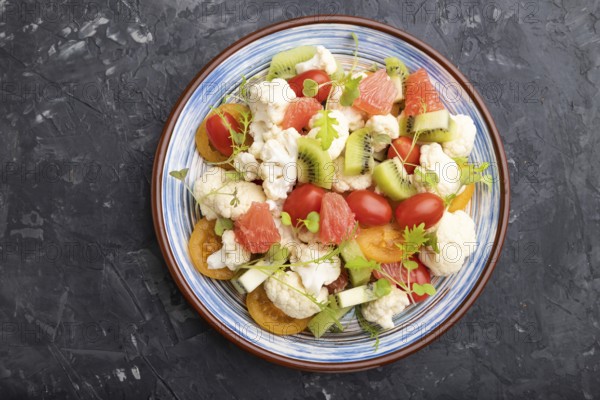 Vegetarian salad of cauliflower cabbage, kiwi, tomatoes, microgreen sprouts on black concrete