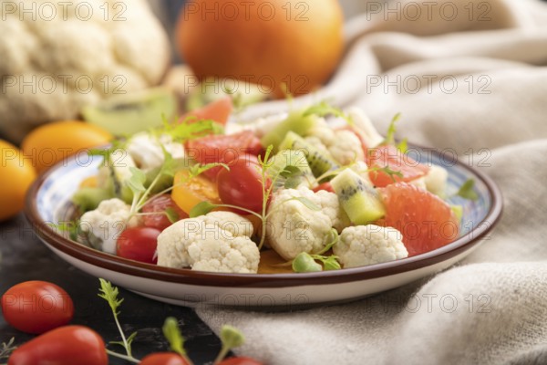 Vegetarian salad of cauliflower cabbage, kiwi, tomatoes, microgreen sprouts on black concrete