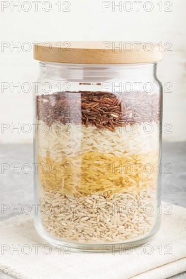 Glass jar with different kinds of rice poured in layers on a gray and white background. side view,