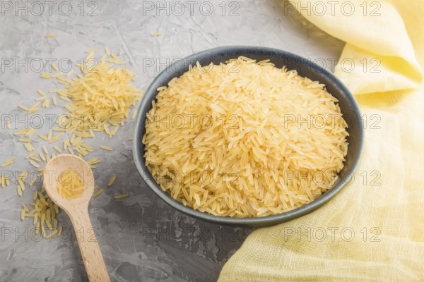 Blue ceramic bowl with raw golden rice and wooden spoon on a gray concrete background and yellow