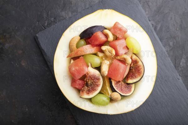Vegetarian fruit salad of watermelon, grapes, figs, pear, orange, cashew on slate board on a black