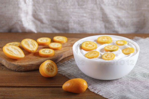 Greek yogurt with kumquat pieces in a white plate on a brown wooden background, close up