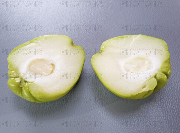 Two halves of a green chuchu with visible white flesh on a grey background, chayote, vegetable,