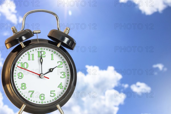 Symbolic image of the time change to summer time: close-up of an alarm clock in front of a blue sky