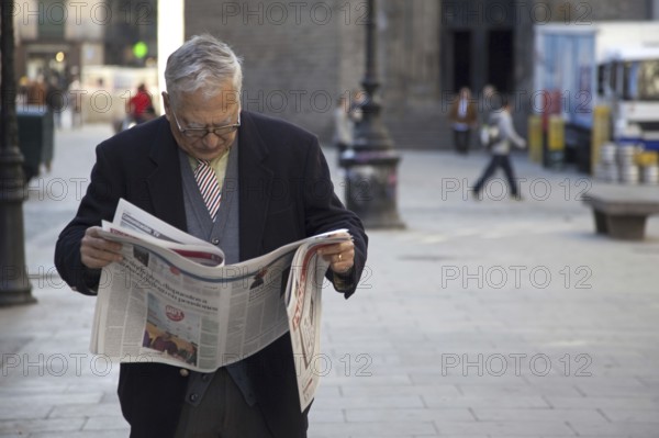 Elderly man reading newspaper in the streets of the old Barri Gòtic, Gothic quarter of Barcelona,