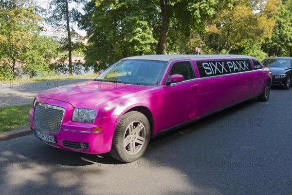 An eye-catching pink limousine parked on the roadside under trees in daylight, stretch limousine,
