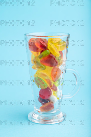 Various fruit jelly candies in drinking glass on blue pastel background. side view, close up