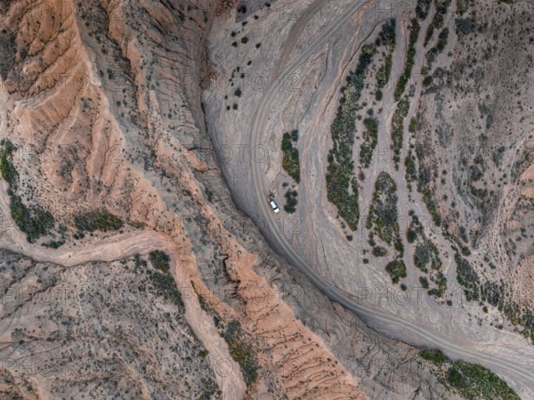 Off-road vehicle on a track in a riverbed, landscape of eroded hills, top-down, badlands, aerial