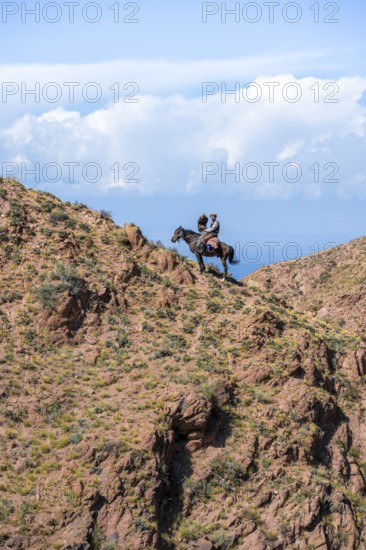 Traditional Kyrgyz eagle hunter with eagle in the mountains, hunting on horseback in front of dry