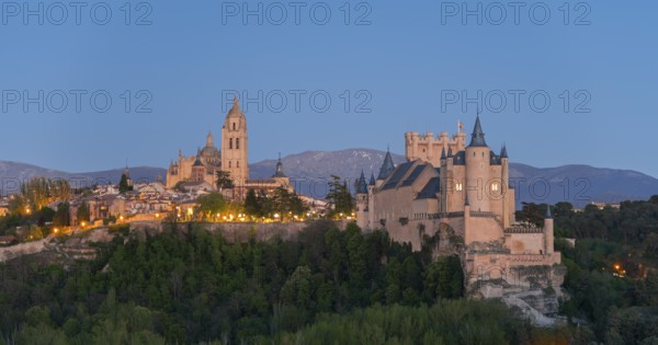 A majestic castle on a hill at dusk with illuminated buildings and a mountain backdrop, Cathedral,