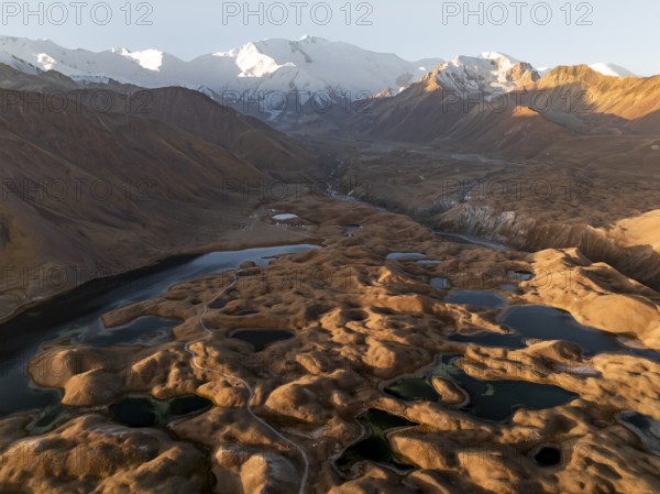 White glaciated and snowy mountain peak Pik Lenin at sunrise, hilly landscape with golden yellow