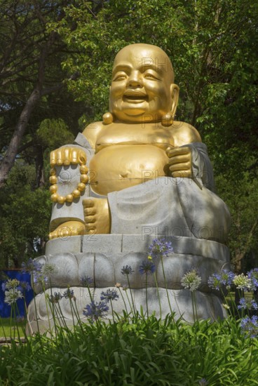 Golden Buddha statue, surrounded by flowers and green nature, radiates peace and spirituality under