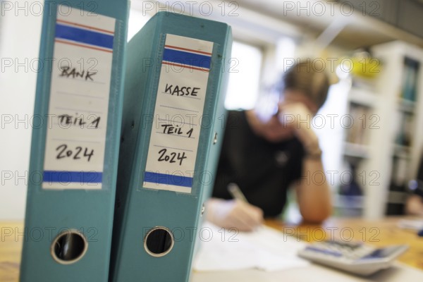 Symbolic photo: A woman sits at a desk in an office with a calculator and file folders and does