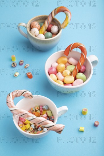 Heap of multicolored caramel candies in cups on blue pastel background. close up, side view