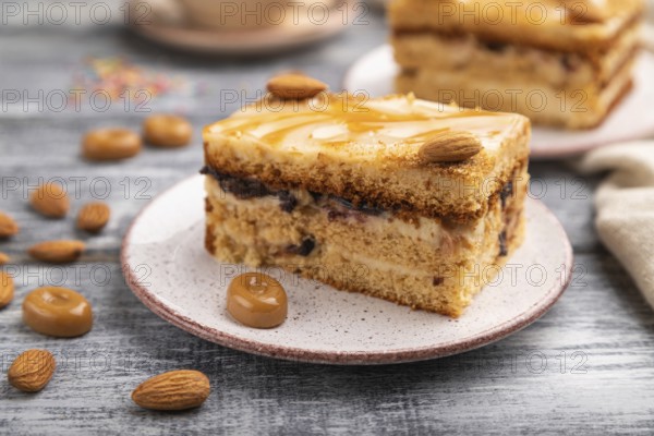 Honey cake with milk cream, caramel, almonds and a cup of coffee on a gray wooden background and