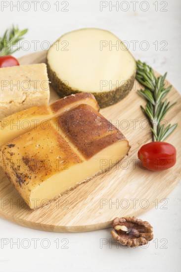 Smoked cheese and various types of cheese with rosemary and tomatoes on wooden board on a white
