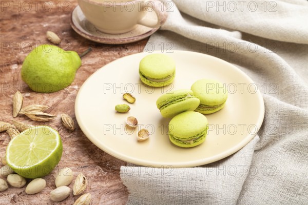 Green macarons or macaroons cakes with cup of coffee on a brown concrete background and linen