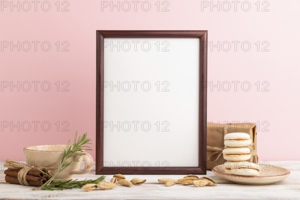 Brown wooden frame mockup with cup of coffee, almonds and macaroons on pink pastel background.