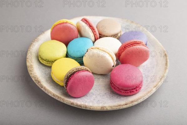 Multicolored macaroons on ceramic plate on gray pastel background. side view, close up, still life.