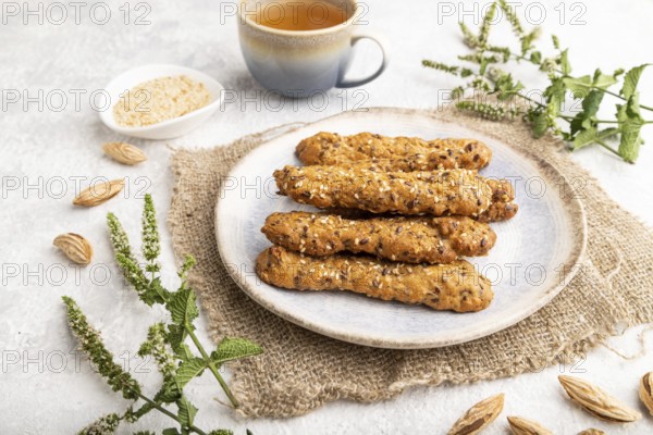 Crumble cookies with seasme and almonds on ceramic plate with cup of green tea and linen textile on