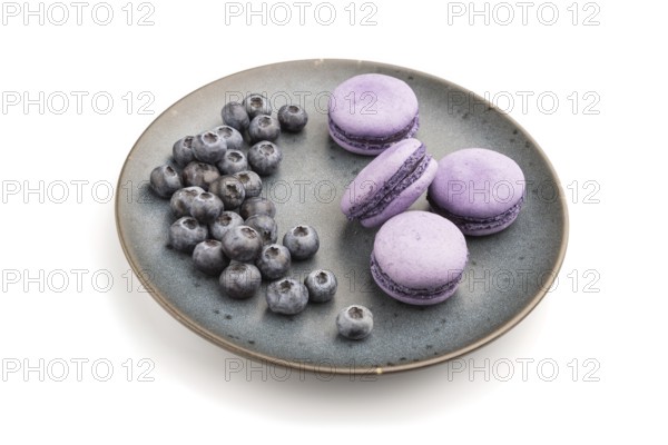 Purple macarons or macaroons cakes with blueberries on ceramic plate isolated on white background.
