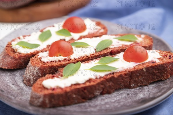 Red beet bread sandwiches with cream cheese and tomatoes on white concrete background and blue