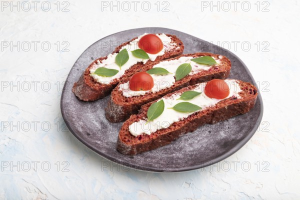 Red beet bread sandwiches with cream cheese and tomatoes on white concrete background. Side view,