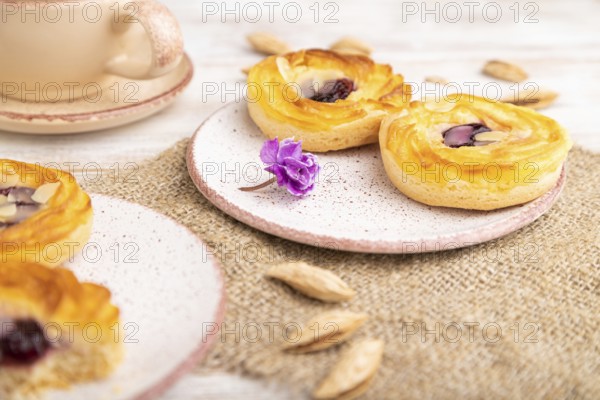 Small cheesecakes with jam and almonds with cup of coffee on a white wooden background and linen