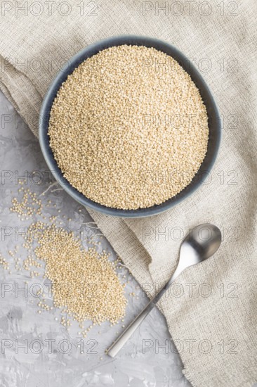 Blue ceramic bowl with raw white quinoa seeds on a gray concrete background and linen textile. Top