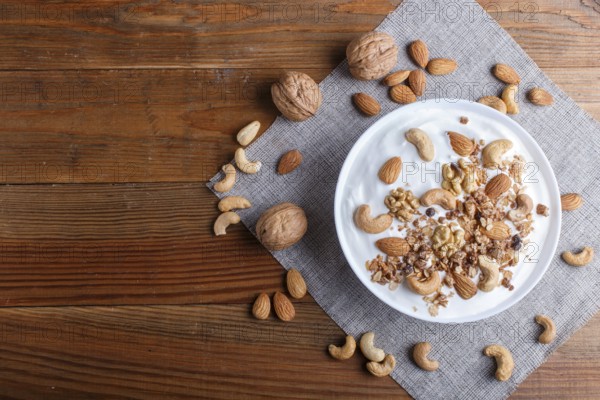White plate with greek yogurt, granola, almond, cashew, walnuts on brown wooden background. top