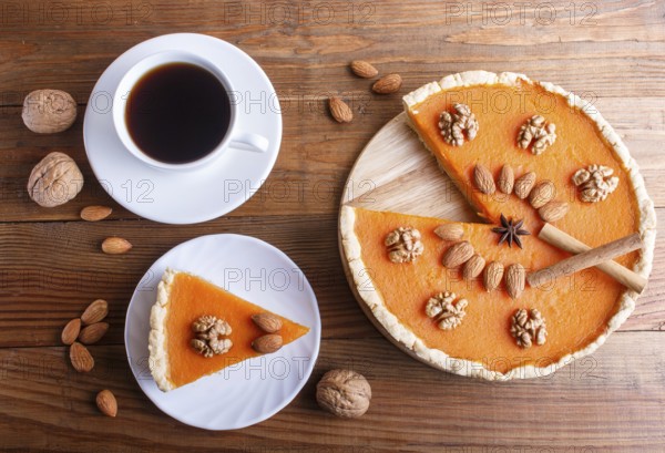 Traditional american sweet pumpkin pie decorated with nuts, on brown wooden background. cup of