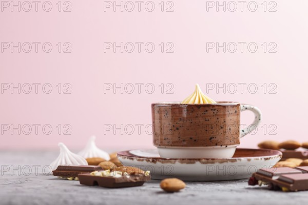 Cup of hot chocolate and pieces of milk chocolate with almonds on a gray and pink background. side