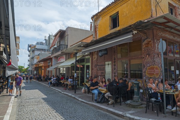 People enjoying food and drinks in outdoor seating along a lively street, Alexandroupoli,