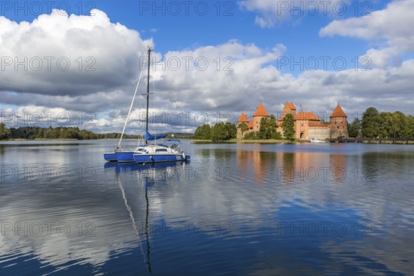 Blue yacht on Galve lake, Lithuania with Trakai castle and cloudy sky on background