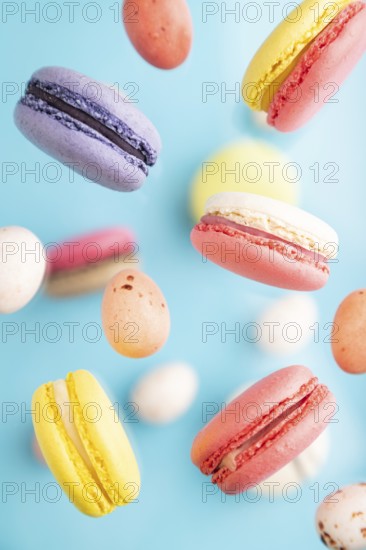 Multicolored flying macaroons and chocolate eggs frozen in the air on blurred blue background. top