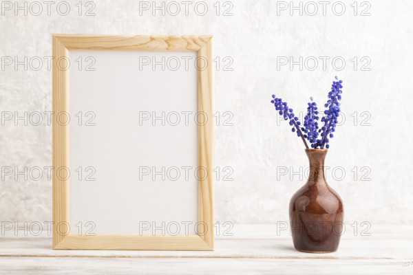 Wooden frame with blue muscari hyacinth flowers in ceramic vase on gray concrete background. side
